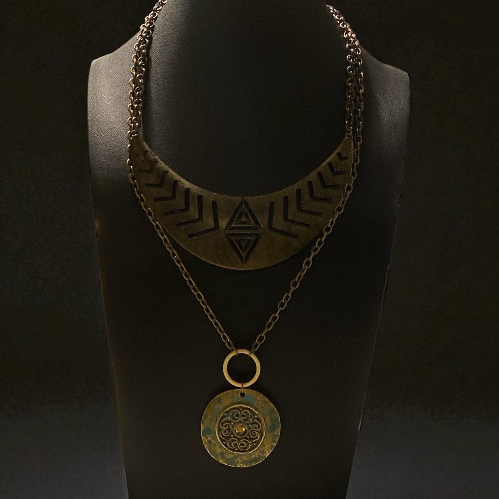 Brass crescent bib doubled with chain holding brass distressed green medallion.